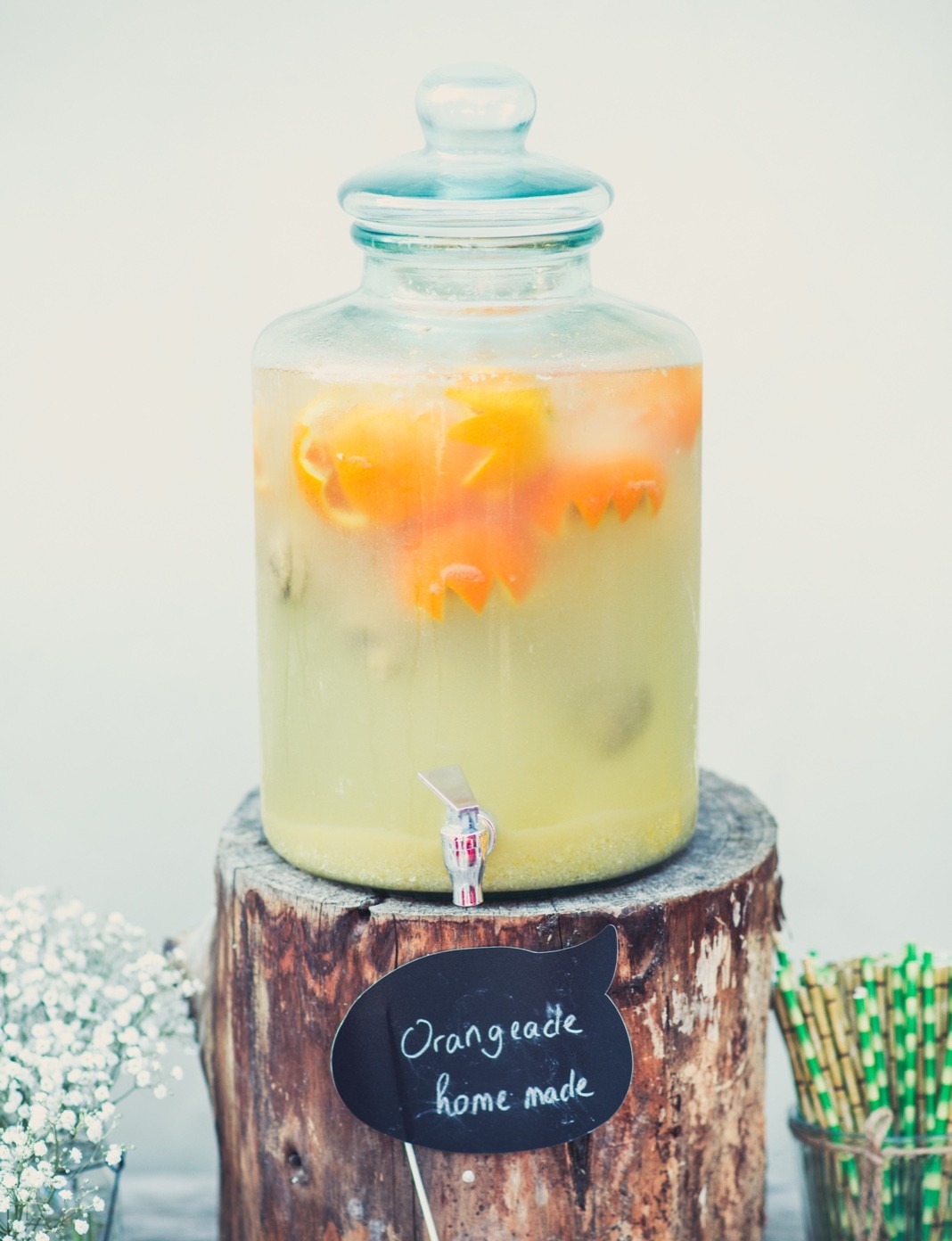 Orangeade maison dans une fontaine en verre posée sur un rondin de bois, gypsophile et pailles colorées — détail d'un brunch de mariage