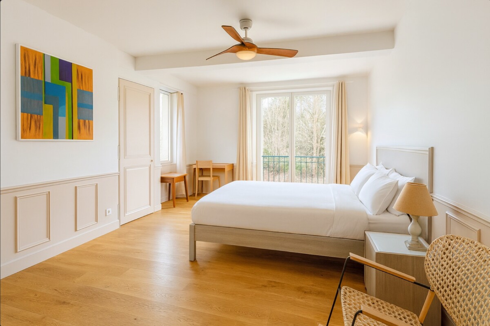 Chambre lumineuse avec boiseries, lit double et grande fenêtre donnant sur la verdure