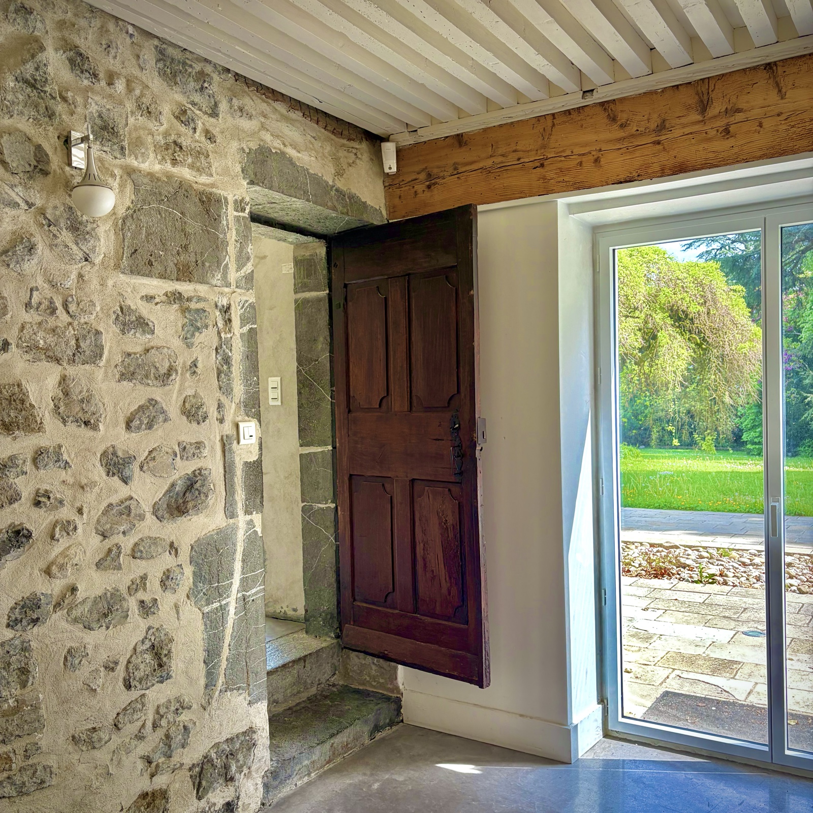 Entrée en pierres apparentes avec porte ancienne en bois et vue sur le parc