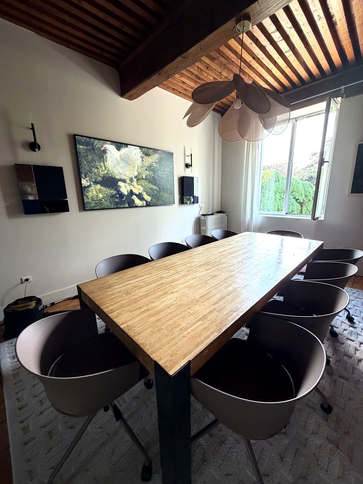 La salle de réunion équipée : table rectangulaire en bois, fauteuils ergonomiques, écran 75 pouces pour visioconférence, suspension design, plafond à poutres anciennes