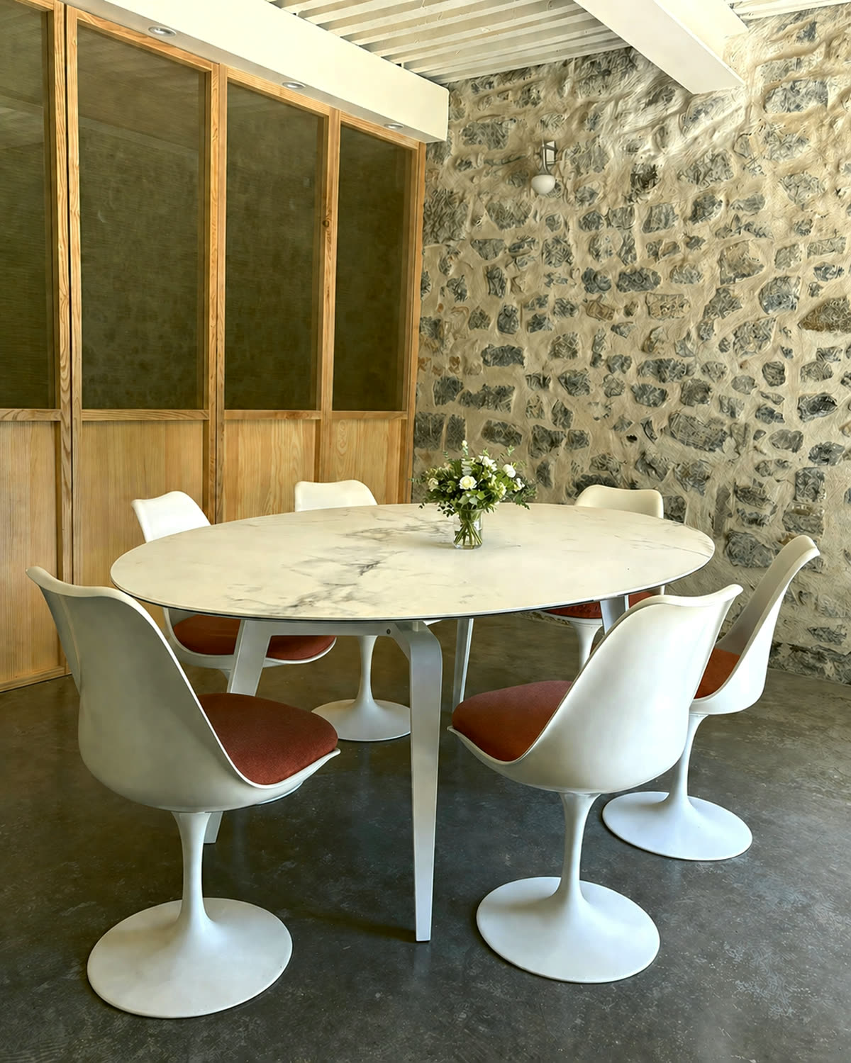 Salle de réunion : table ovale en marbre, six chaises Tulip blanches, mur en pierres apparentes